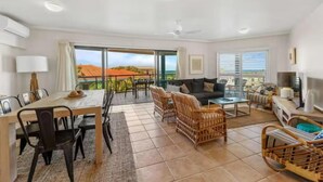 A spacious living area with a dining table, chairs, a sofa, and a TV. - The Cove Yamba (Yamba)