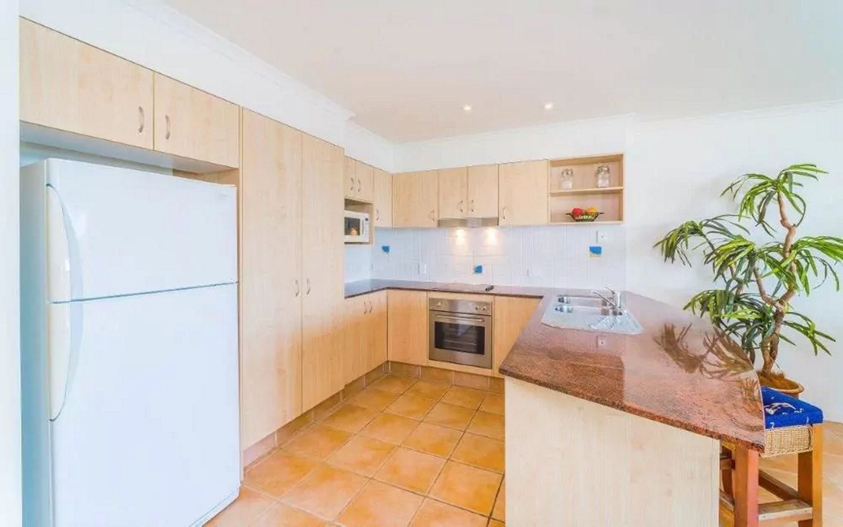 A compact kitchen with light wooden cabinets, a built-in oven, a microwave, and a sink.