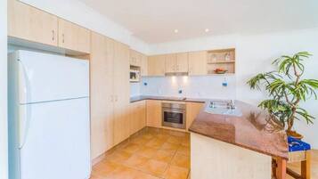 A compact kitchen with light wooden cabinets, a built-in oven, a microwave, and a sink.