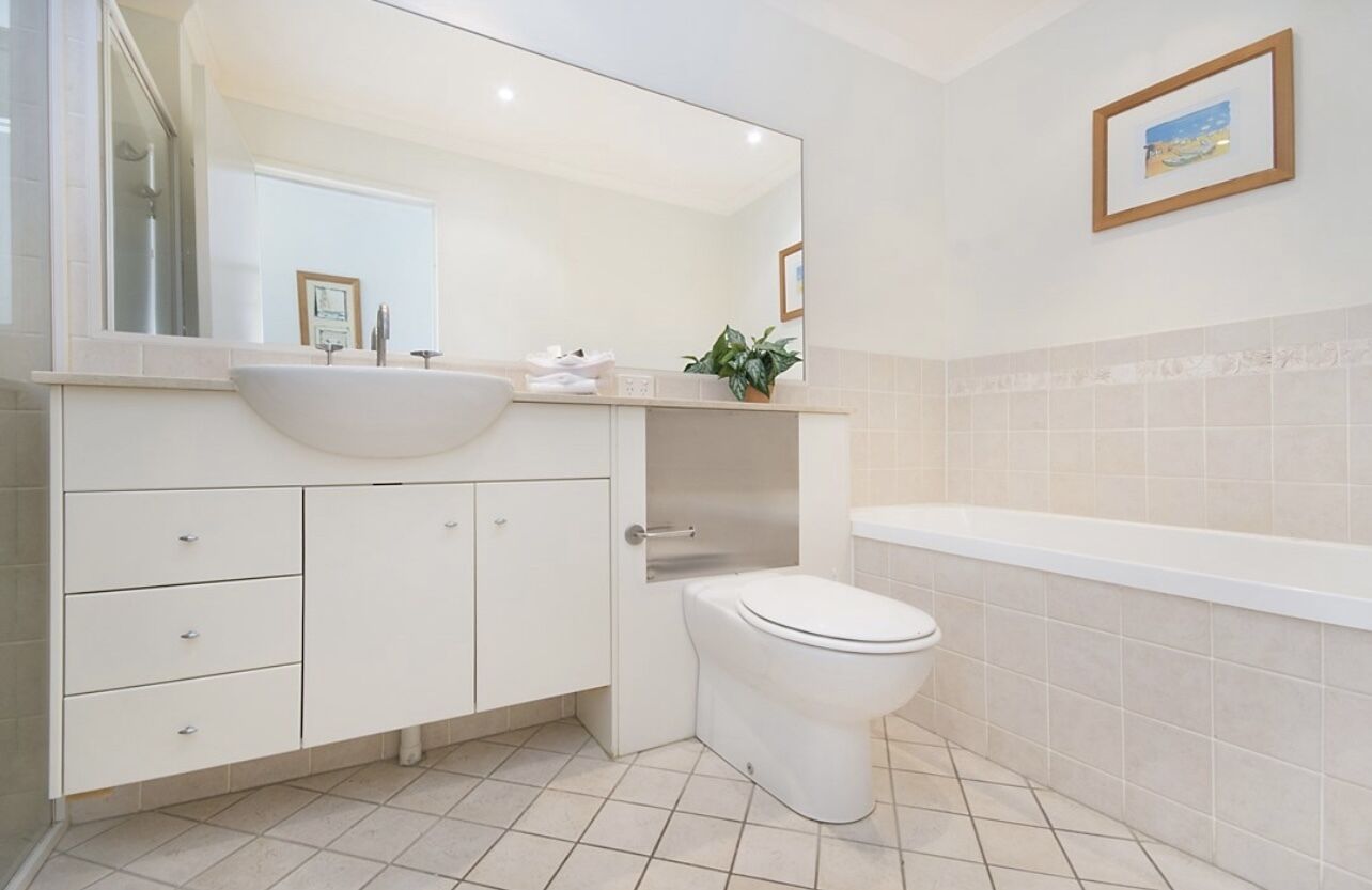 Un baño moderno con un lavamanos, espejo y retrete blancos.