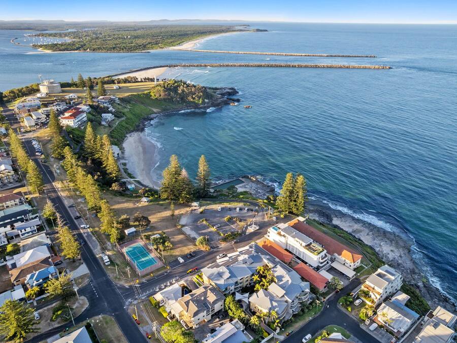 An aerial view of a coastal residential area with houses, a beach, and a marina.