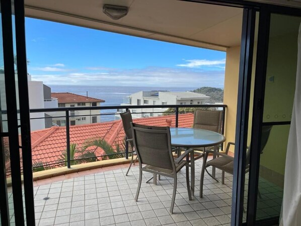 Un balcón con mesa y sillas, que ofrece vistas al mar y edificios.