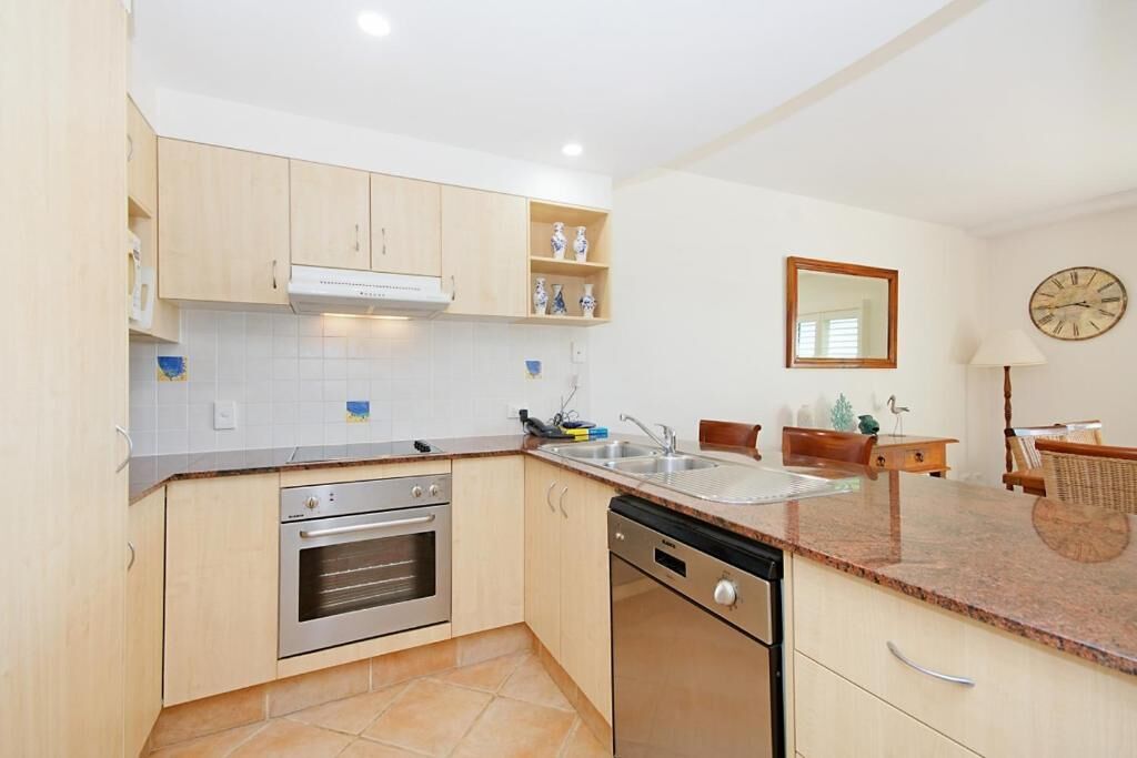 A modern kitchen with light wood cabinets, a built-in oven, a dishwasher, and a granite countertop.