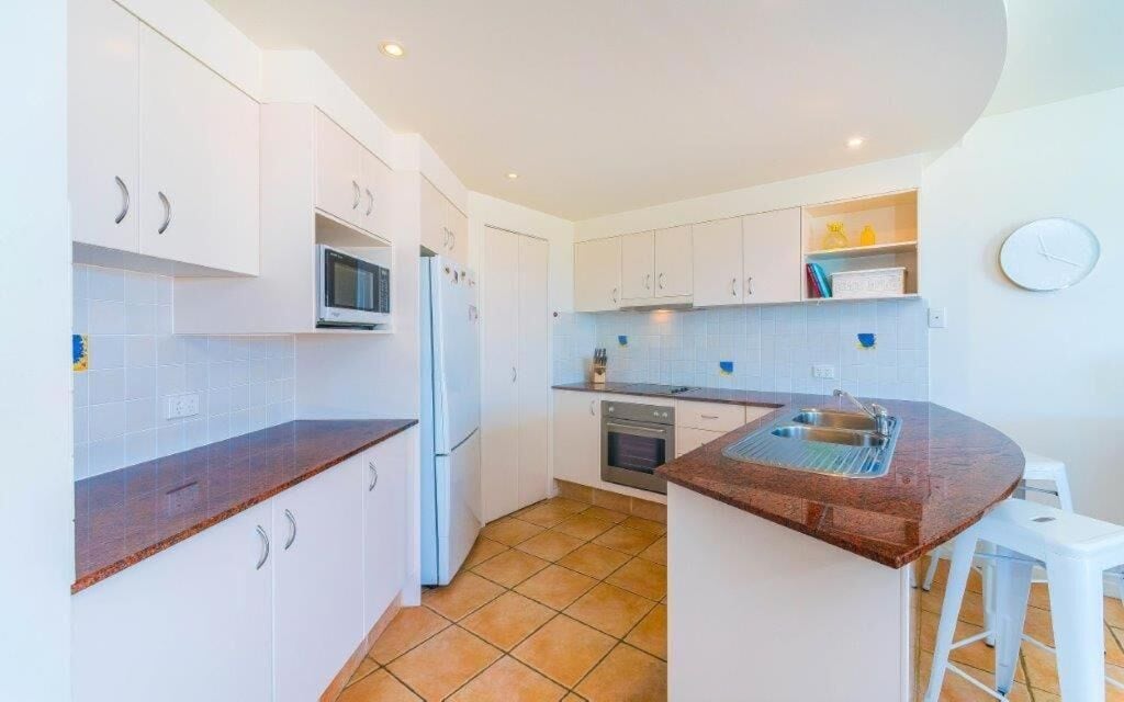 A compact kitchen with white cabinets, a microwave, a refrigerator, an oven, and a sink.