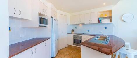 A compact kitchen with white cabinets, a microwave, a refrigerator, an oven, and a sink.