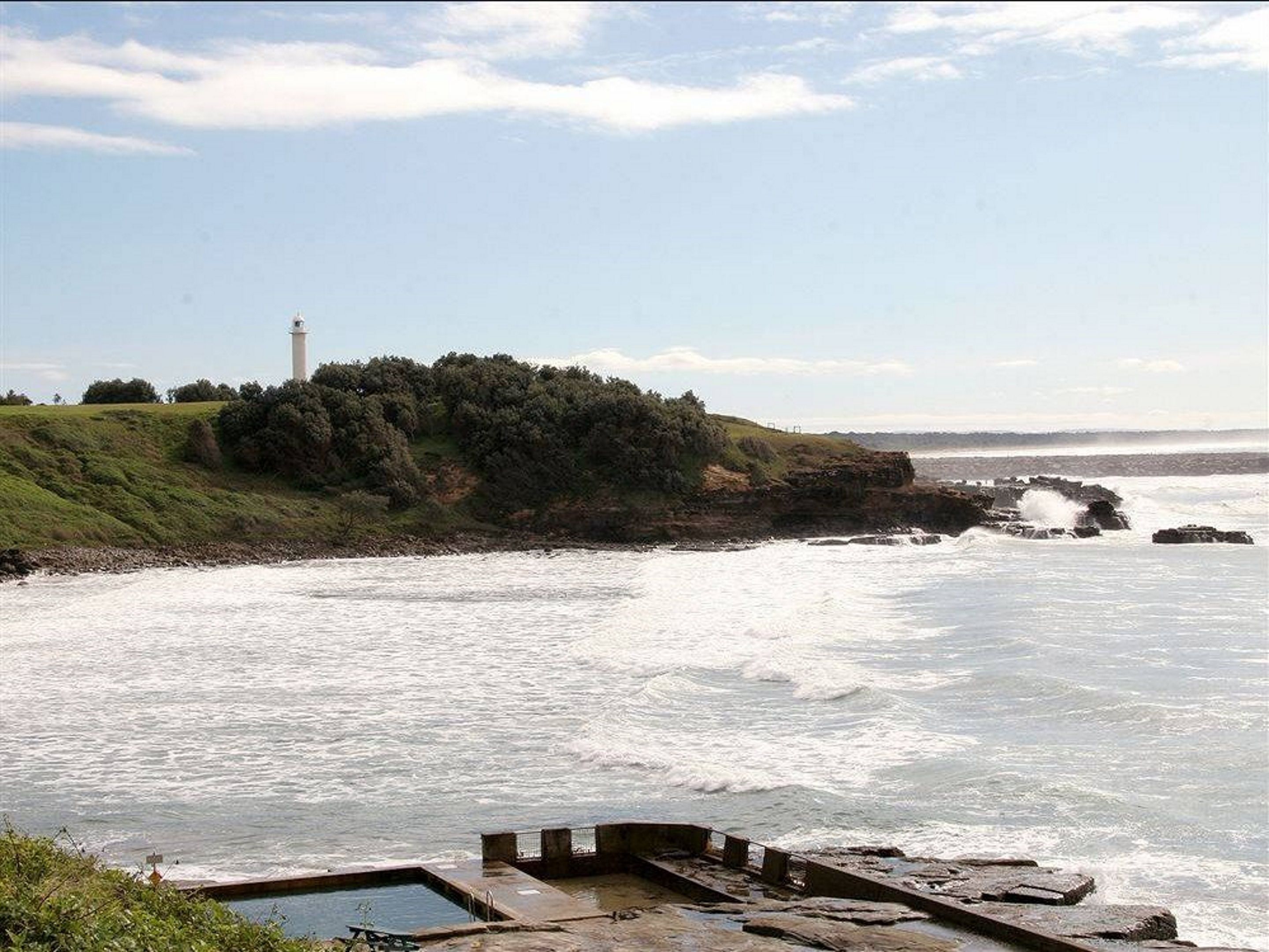A coastal landscape with a lighthouse, rocky shoreline, and a grassy hill.