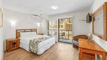 A bedroom with a bed, wooden nightstand, and a desk with a chair. There is a balcony with a chair and a table.