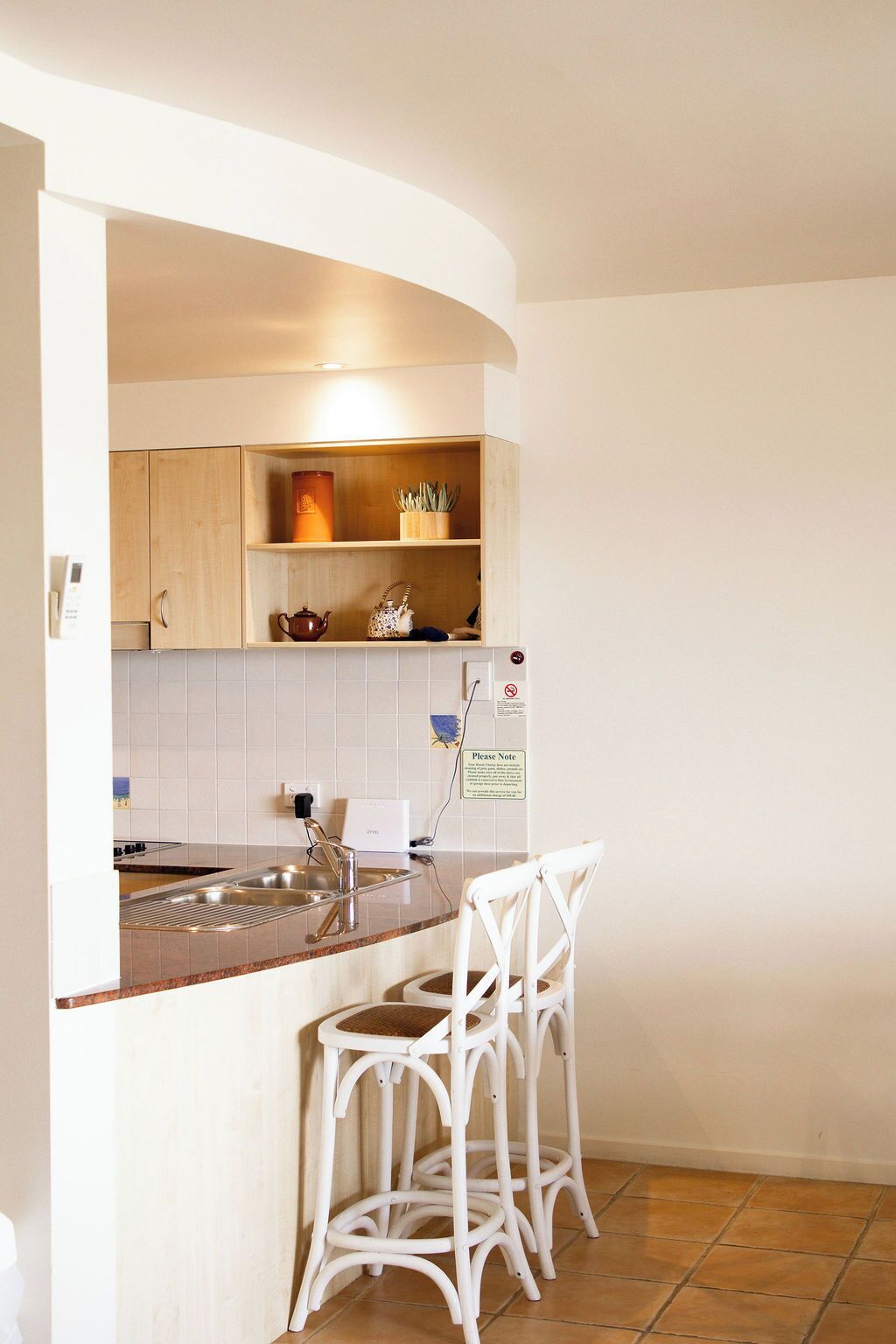 A kitchen with a built-in island, white bar stools, and a tiled backsplash.
