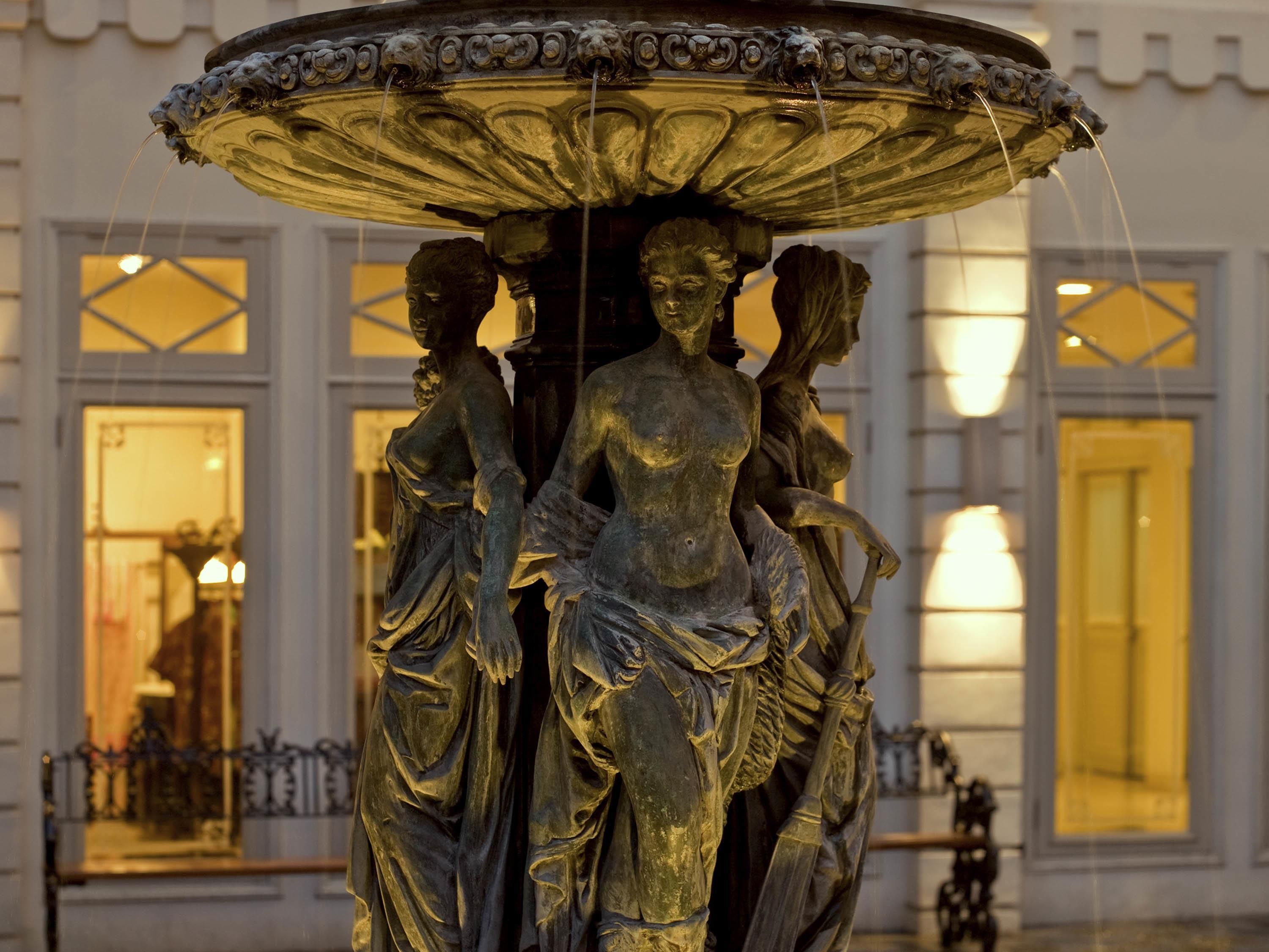A bronze statue of three figures with a fountain above them.