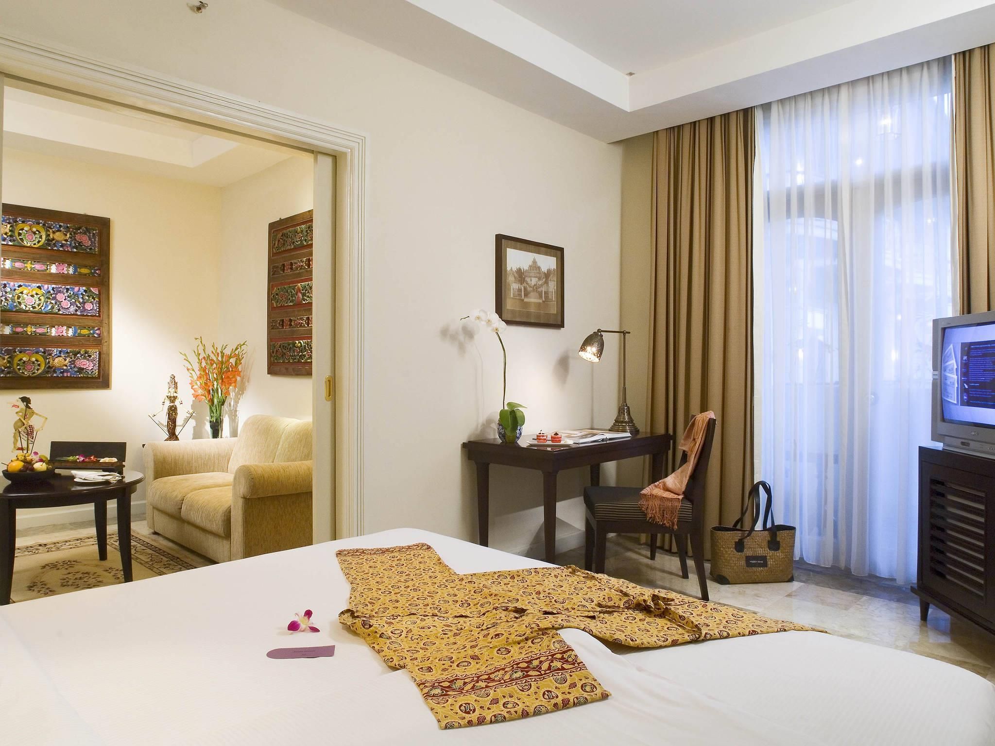 Habitación de hotel con cama, escritorio, silla, televisor y ventana con cortinas.