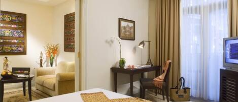 Habitación de hotel con cama, escritorio, silla, televisor y ventana con cortinas.