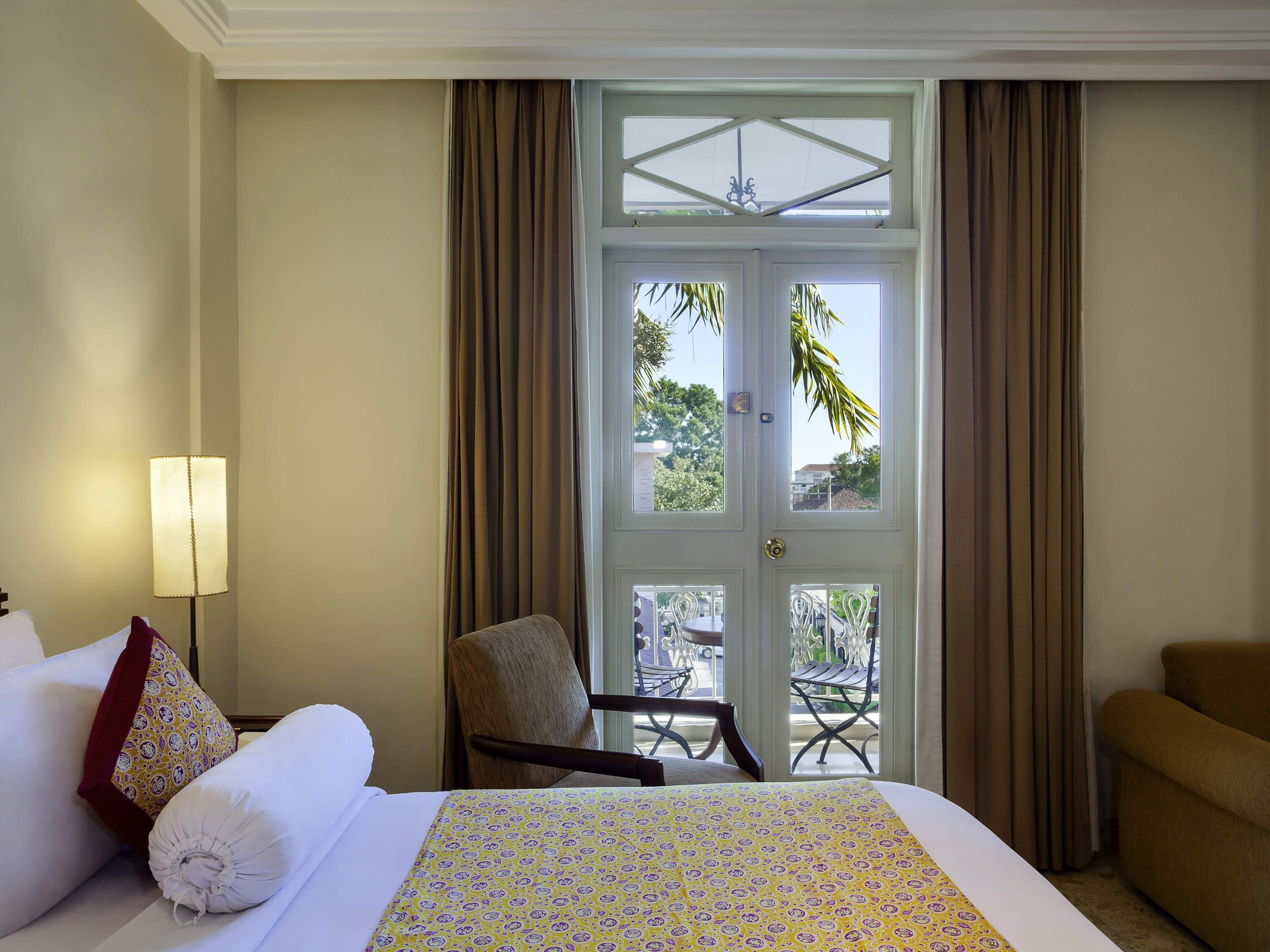 A hotel room with a bed, a chair, a table, and a view through a door.