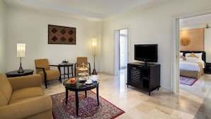 Une chambre d’hôtel comprenant un canapé, des fauteuils, une table basse, une télévision, un minibar et un lit agrémenté d’un tapis à motifs.