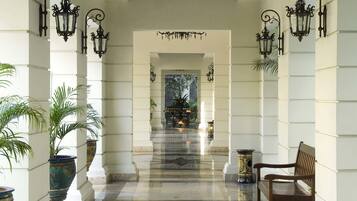 A corridor with ornate black wall sconces, a marble floor, and a bench on the right.