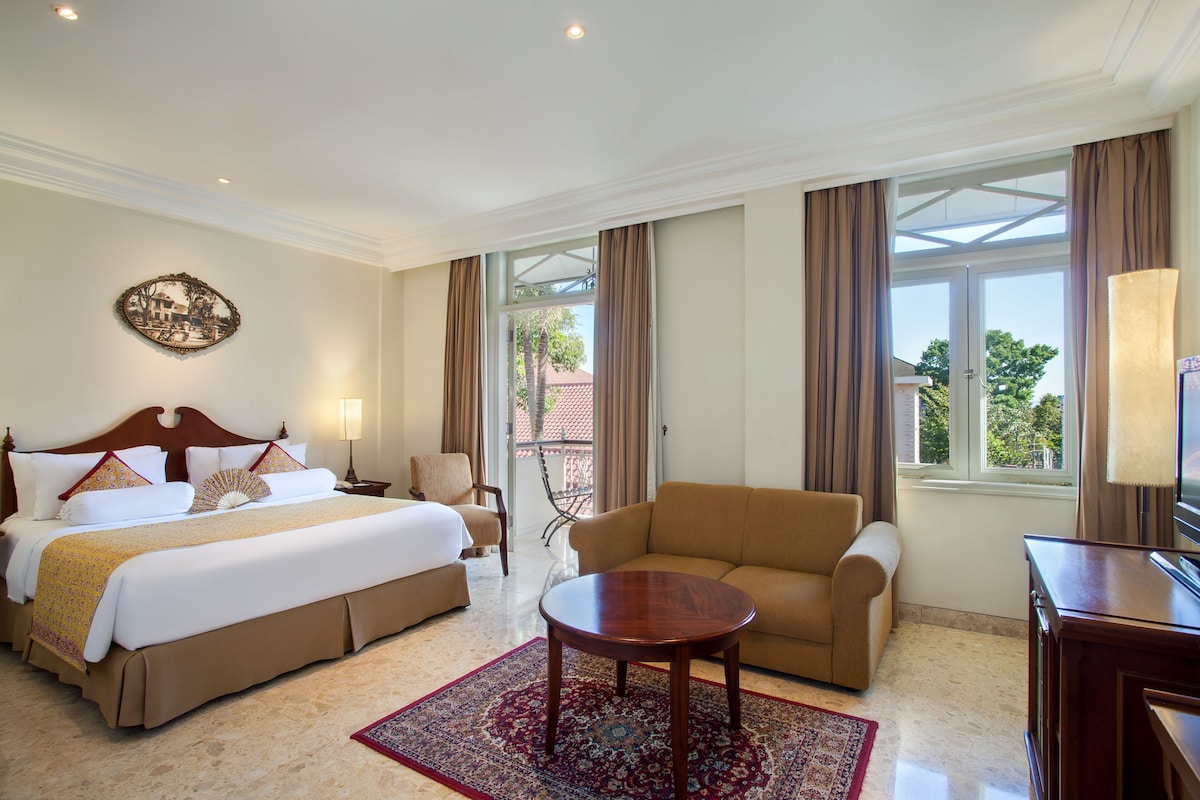 A hotel room with a large bed, a sofa, a small table, and a TV.