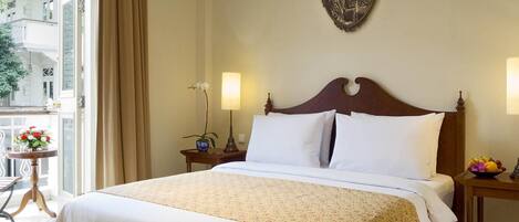 Habitación de hotel con una cama grande, dos mesitas de noche, una pequeña mesa con un jarrón de flores y un cuadro colgado en la pared.