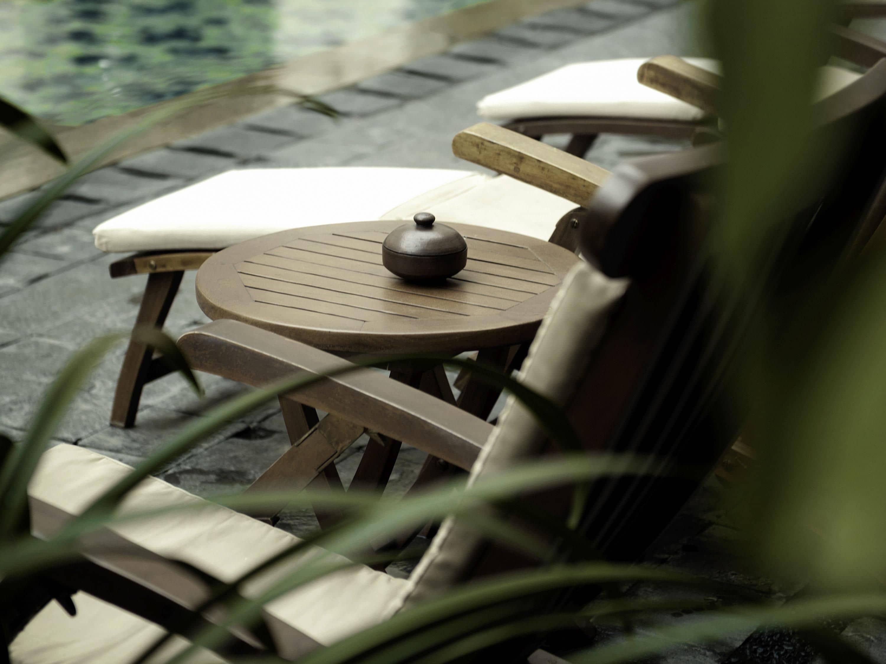 A round wooden table with a black object on it, surrounded by wooden chairs with white cushions.