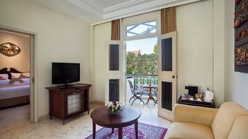 A hotel room with a bed, a TV, a coffee table with a vase, a sofa, and a balcony with a table and chairs.