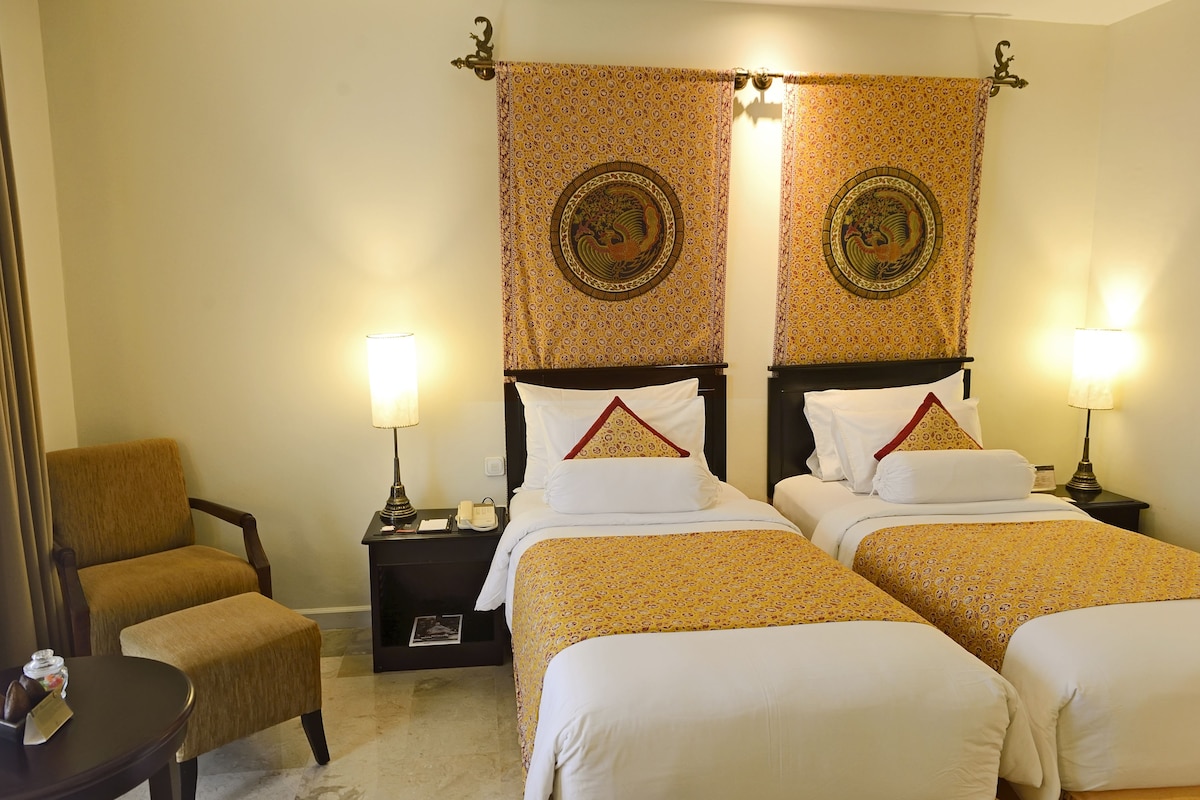A hotel room with two beds, a chair, a nightstand, and a lamp.