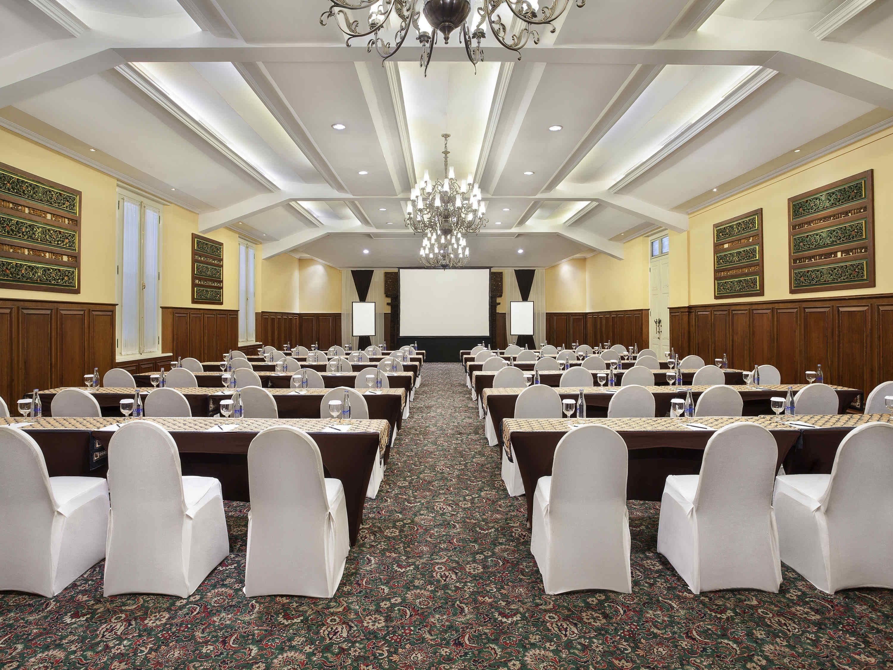 A conference room with rows of tables, chairs, and a projector screen.