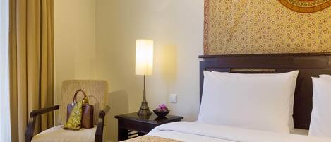 A hotel room with a bed, a chair, a nightstand, a lamp, and a wall with a decorative emblem.