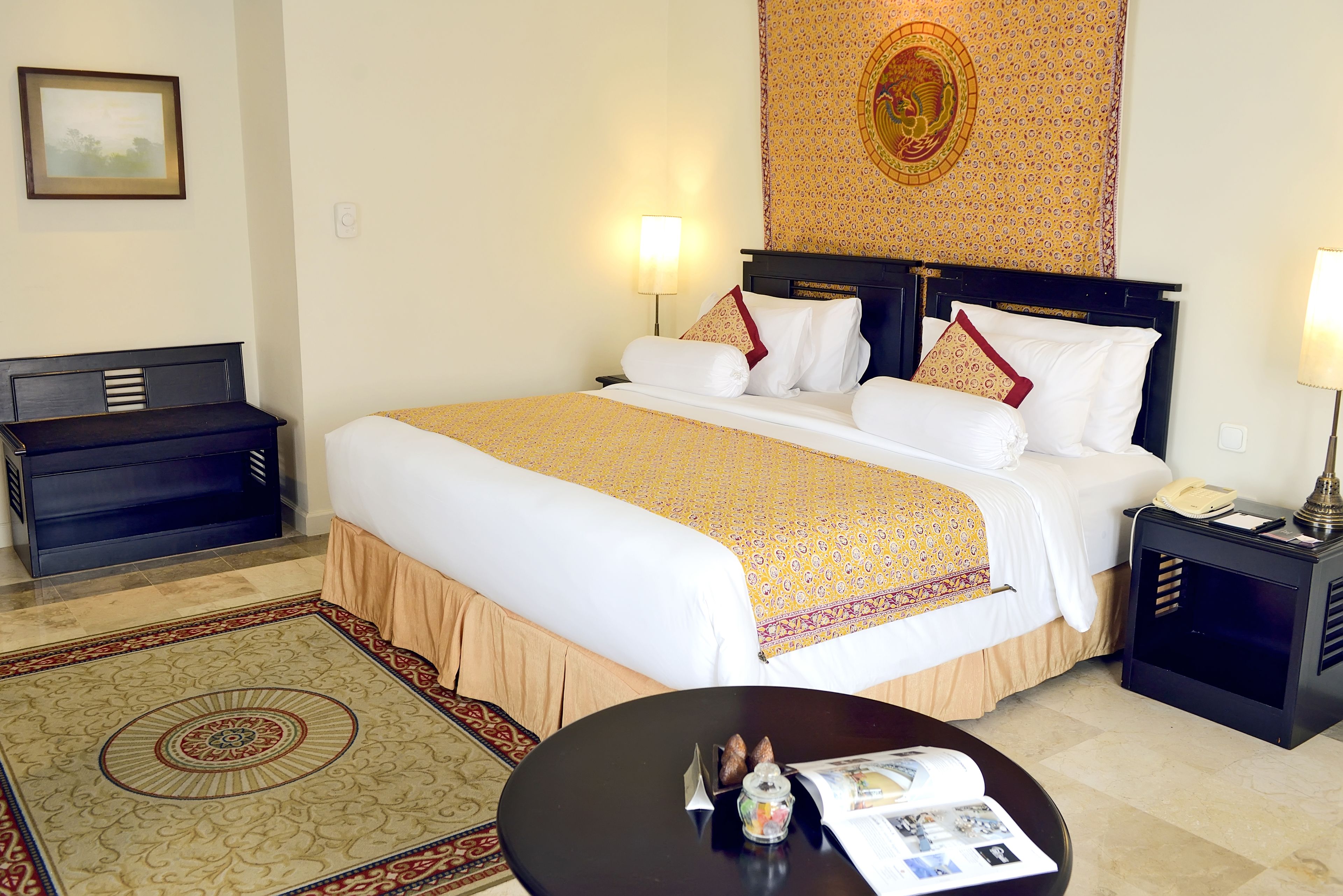 A hotel room with a large bed, bedside tables, a desk, and a patterned rug.
