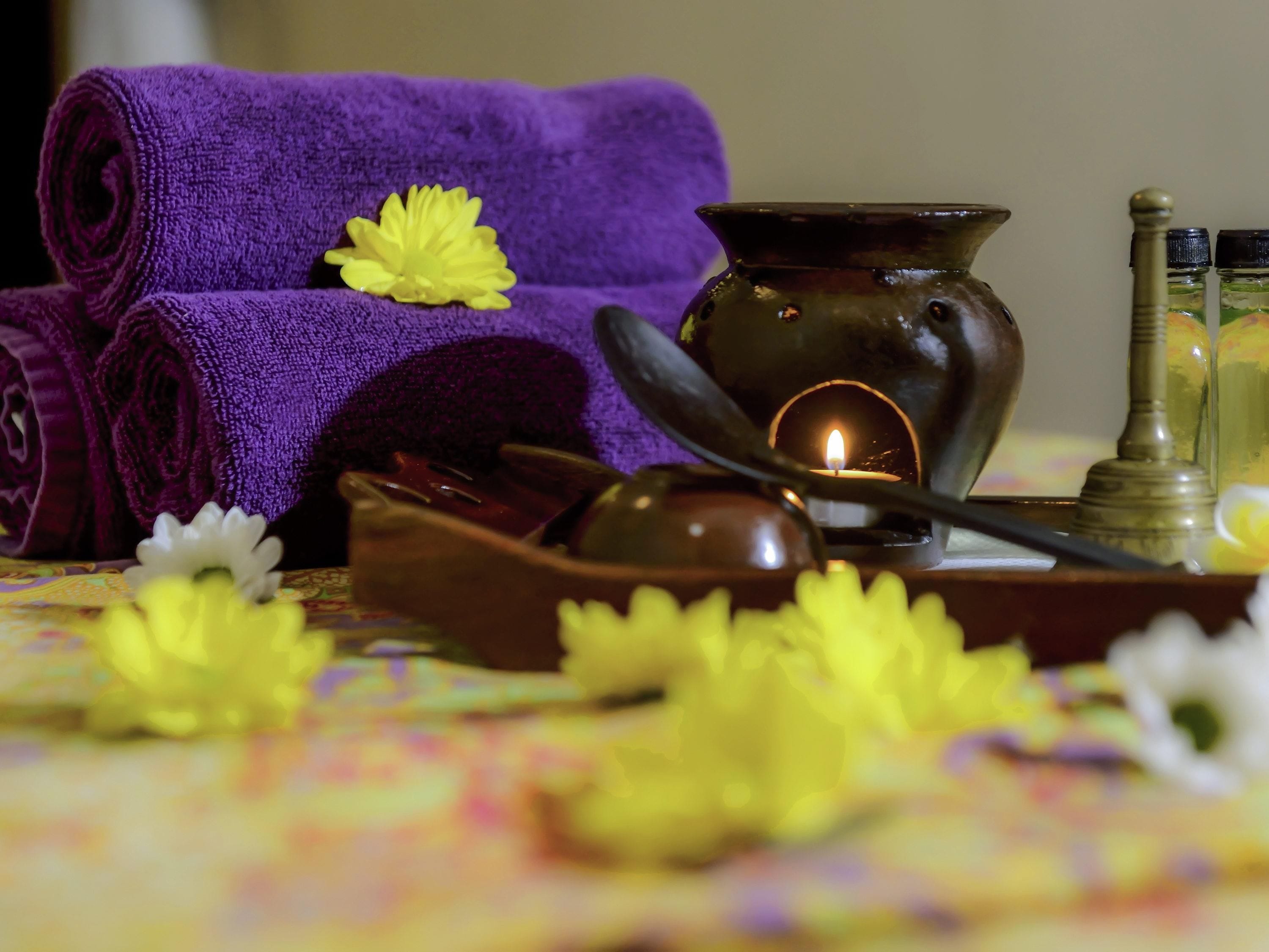 A spa setting with rolled towels, a candle, and essential oils on a table.