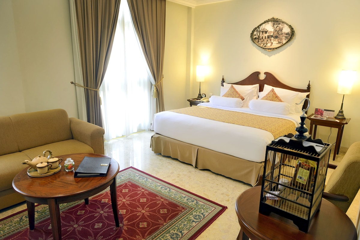 A hotel room with a bed, a sofa, a coffee table, a nightstand, and a lamp.
