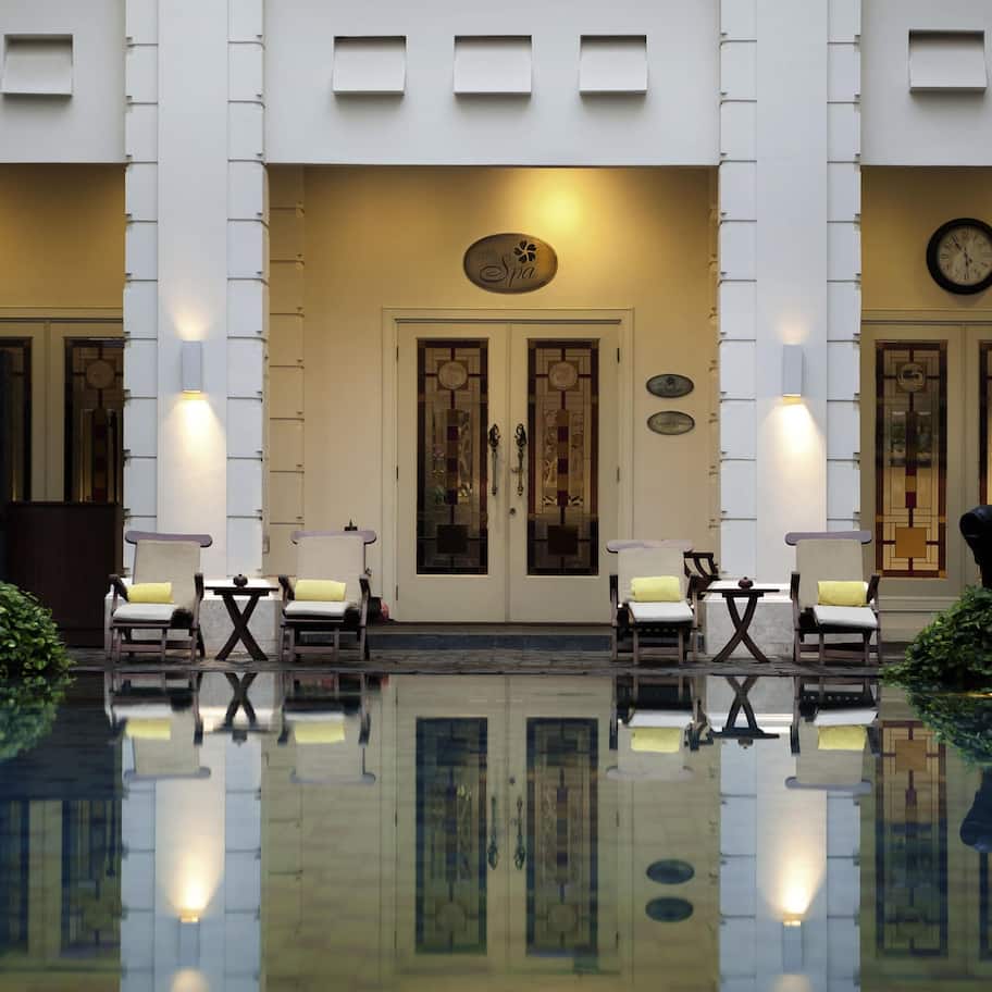 A hotel entrance with a reflective pool, two doors with intricate designs, and a clock on the wall.