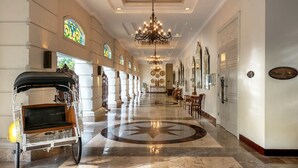 Un vaste hall d’hôtel, avec un sol en marbre, des lustres et un attelage.
