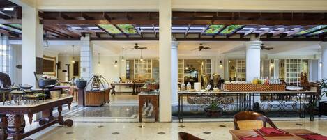 A spacious lobby with high ceilings, large windows with stained glass, and a central seating area with tables and chairs.