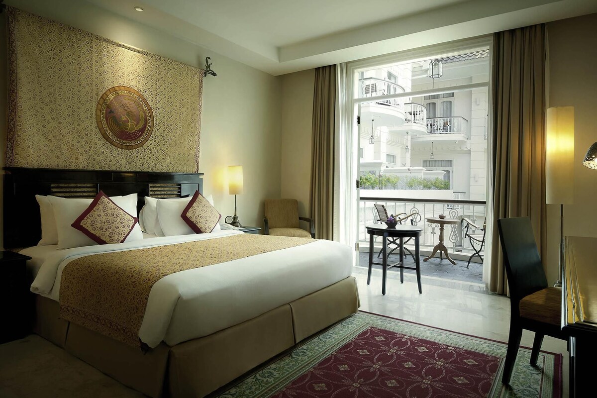 Ein Hotelzimmer mit einem großen Bett, einem Balkon mit Tisch und Stühlen und Blick auf das äußere Erscheinungsbild des Gebäudes.