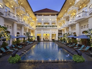A hotel with a central pool, multiple balconies, and outdoor seating areas.