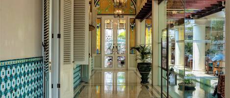 A spacious hallway with a polished marble floor, a grand chandelier, and a staircase with a glass railing.
