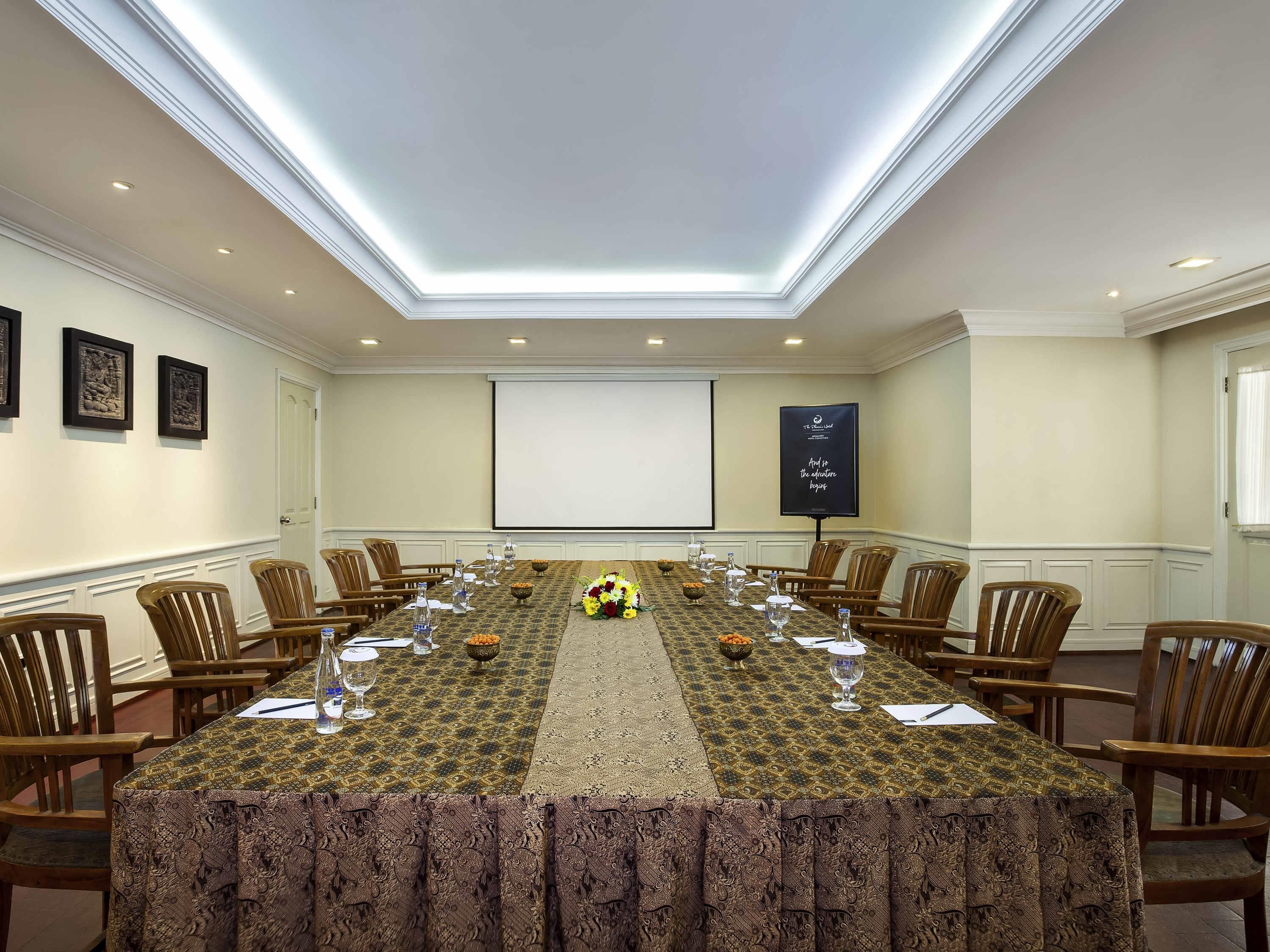 Un salón de conferencias con una larga mesa, sillas, una pantalla de proyector y un cartel motivacional.