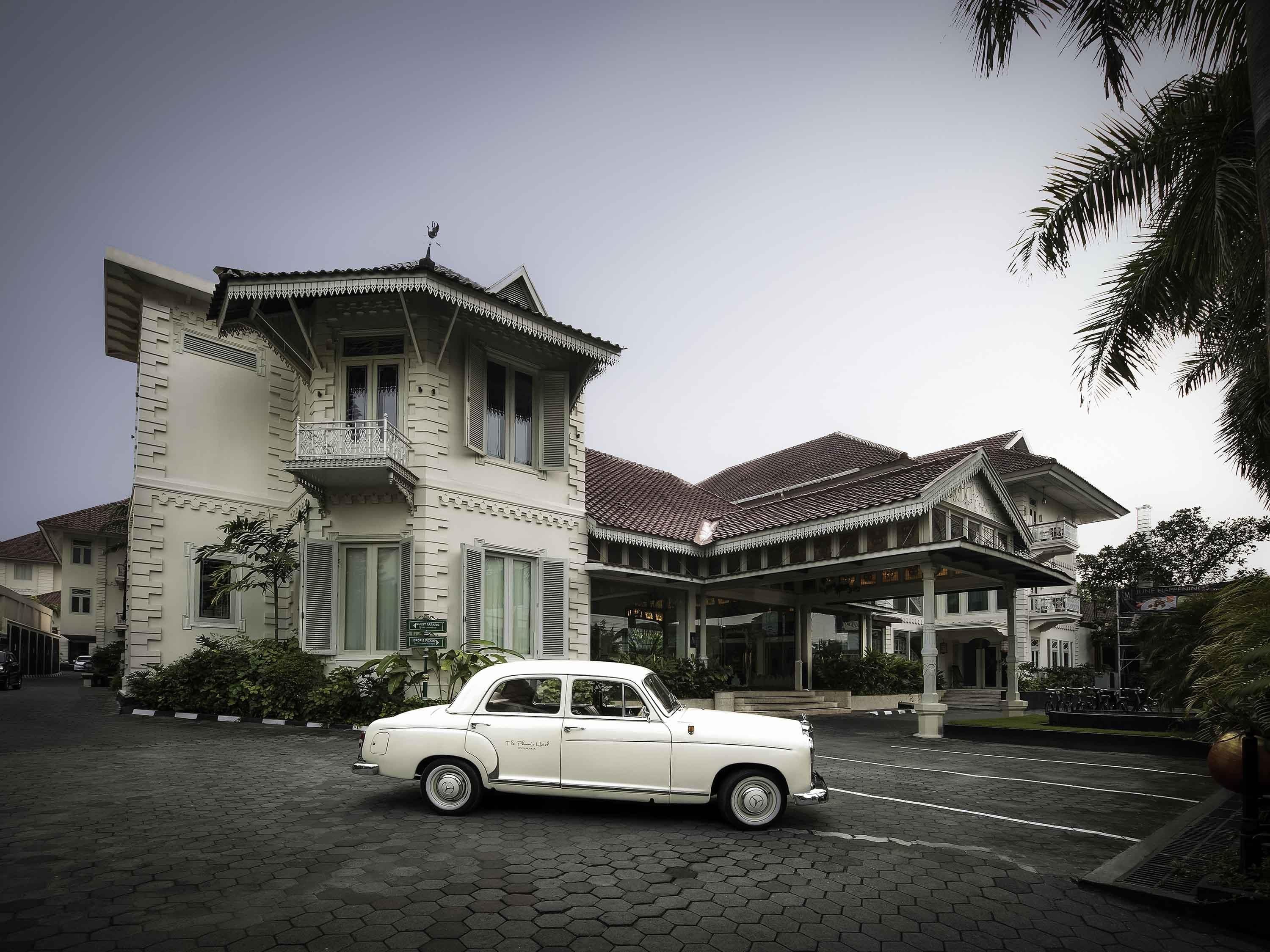A classic white car parked in front of a traditional building with a tiled roof and ornate balcony railings.