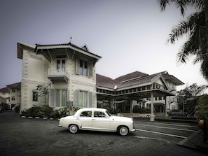 A classic white car parked in front of a traditional building with a tiled roof and ornate balcony railings. - The Phoenix Hotel Yogyakarta - Handwritten Collection (Yogyakarta)