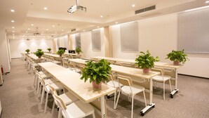 A conference room with multiple tables and chairs, equipped with a projector, and decorated with potted plants. - ibis Tianjing Teda (Tianjin)