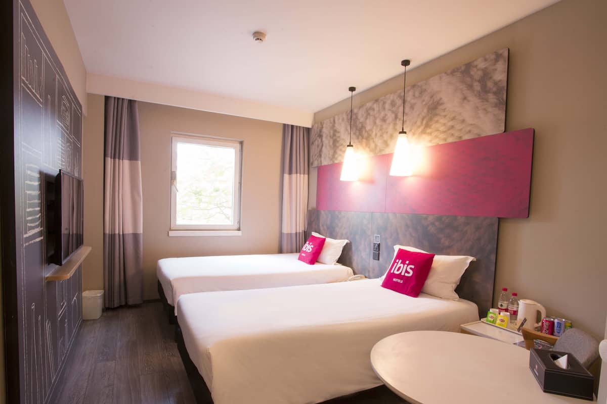 A hotel room with two beds, a small table, and a TV.