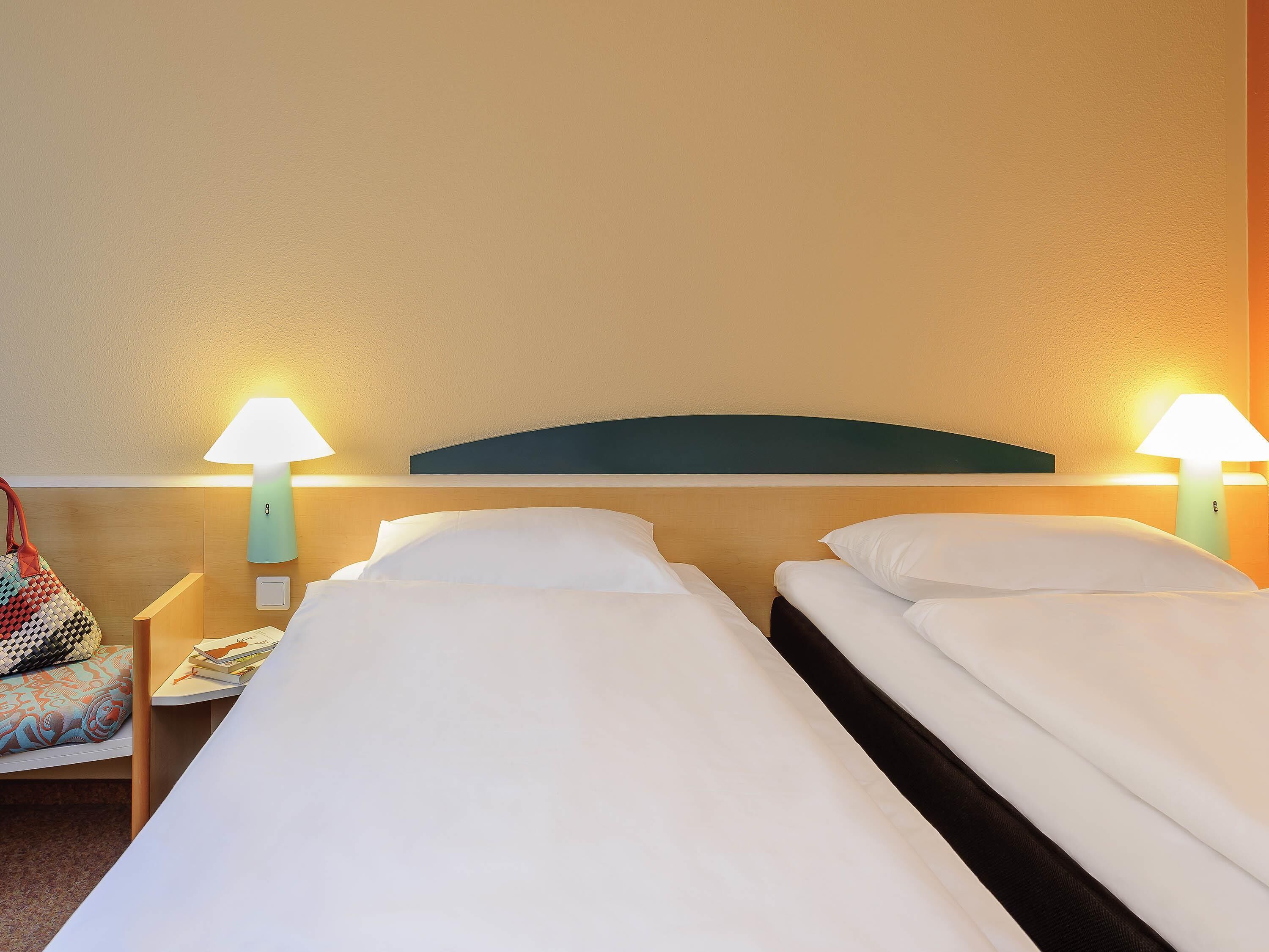 Habitación de hotel con dos camas, una mesita de noche, una lámpara y una silla.