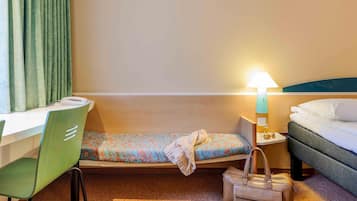 A hotel room with a bed, a desk, a chair, a bedside table with a lamp, and a handbag on the floor.