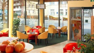 A cafe with yellow chairs, a table with apples, and a TV screen.
