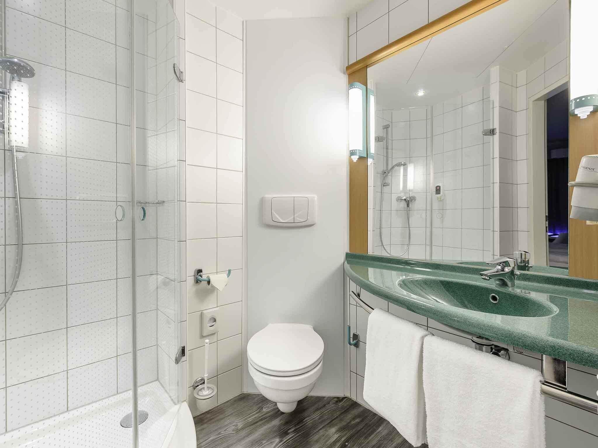 Un baño moderno con cabina de ducha de vidrio, inodoro, lavamanos con encimera verde y espejo.