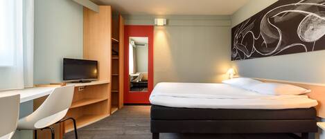 Habitación de hotel con cama, escritorio con silla, televisión y un cuadro abstracto grande en la pared.