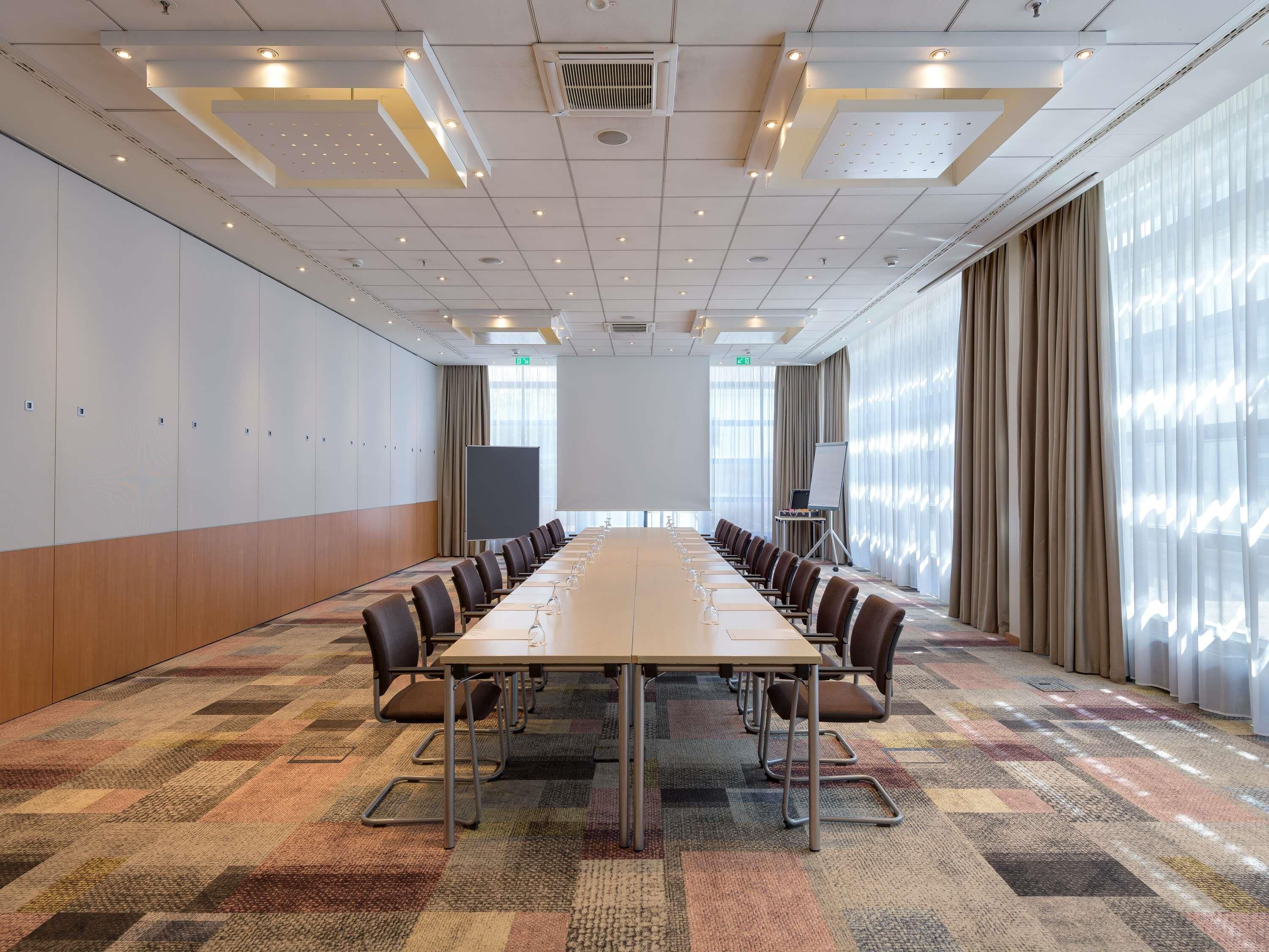 A conference room with a long table, chairs, a projector screen, and a whiteboard.