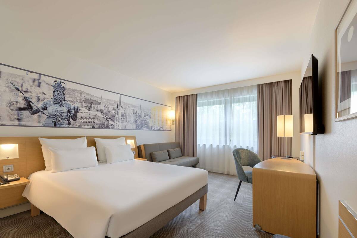 Ein Hotelzimmer mit einem großen Bett, einer Schlafcouch, einem Schreibtisch und einem Fernseher.