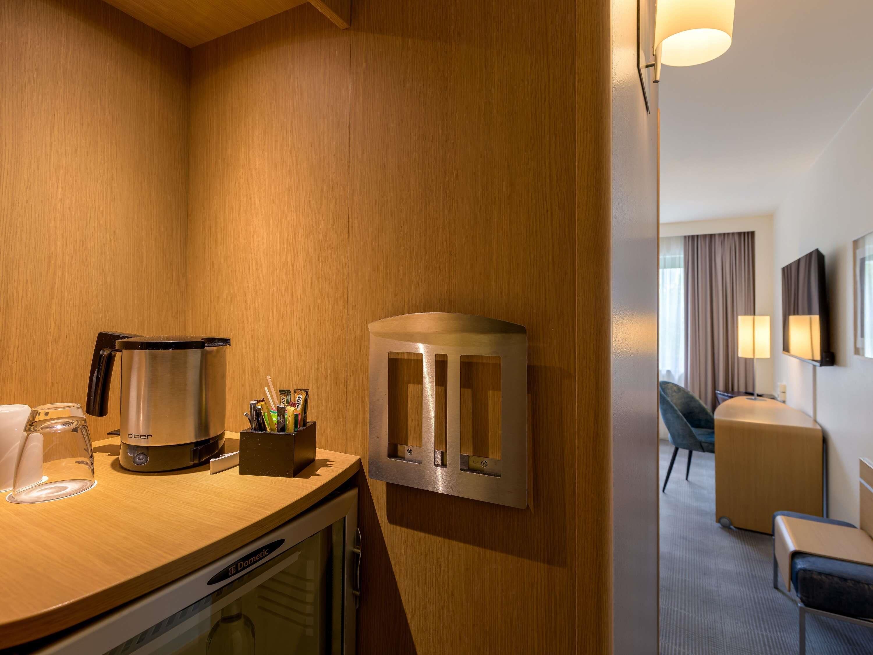 A hotel room with a wooden wall, a coffee maker, a glass, and a small table with a cup holder.