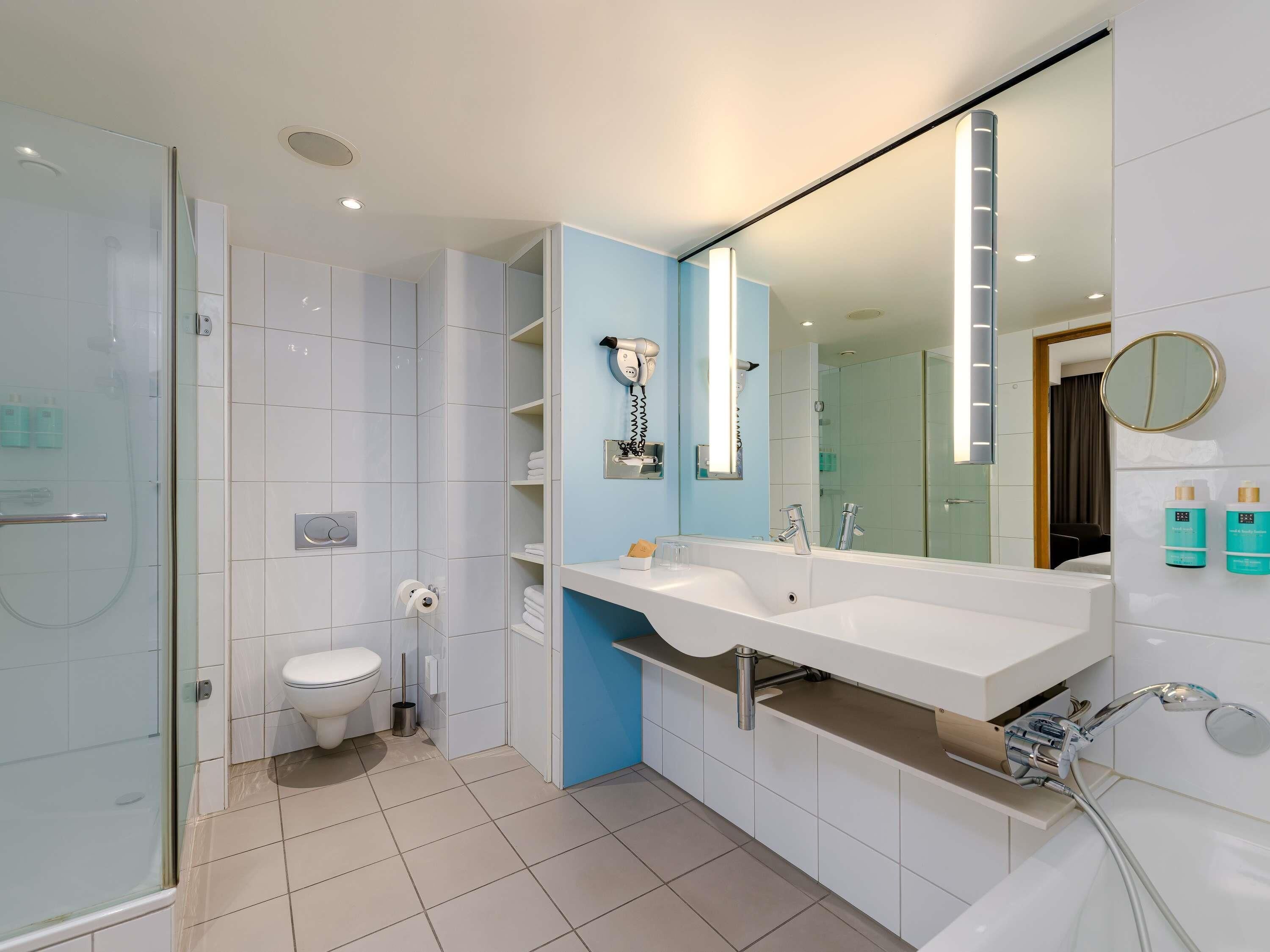 A modern bathroom with a glass shower enclosure, a white sink with a large mirror, and a toilet.