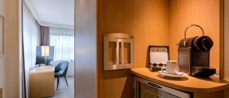 A hotel room with a minibar, a coffee machine, a television, and a seating area with a chair and a desk.