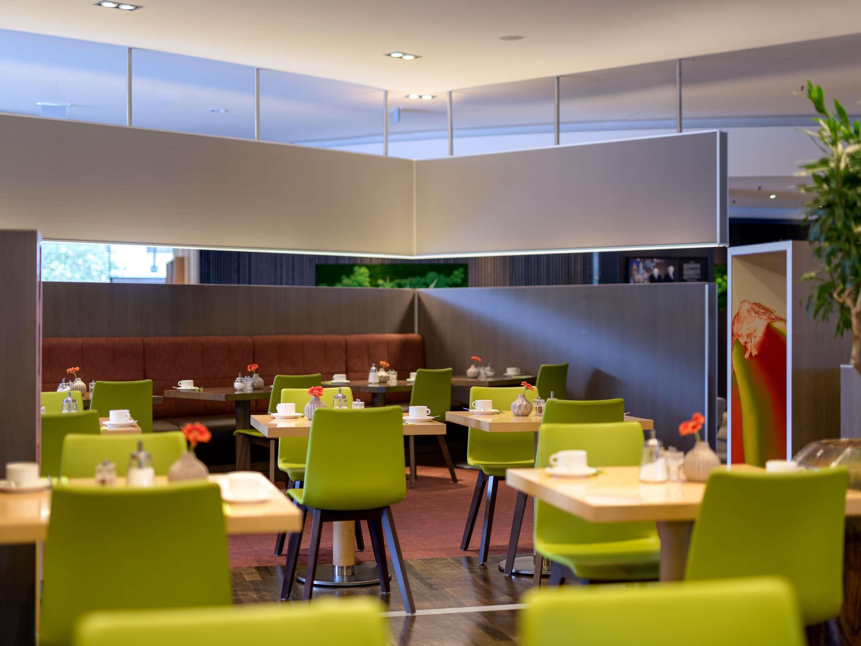 A modern dining area with booths and tables, green chairs, and a television screen.